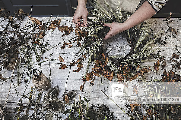 Woman making a small winter wreath of dried plants  brown leaves and twigs  and seedheads.
