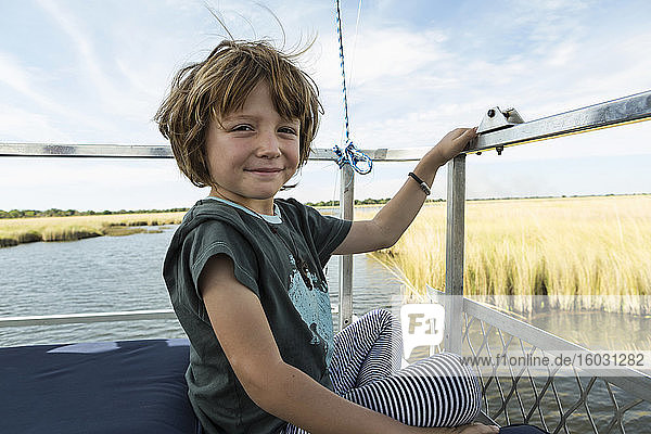 A five year old boy seated on a boat on water.