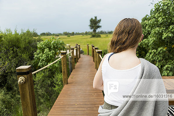 Rückansicht eines dreizehnjährigen Mädchens  das auf einem Holzpfad in einem Camp auf Safari geht