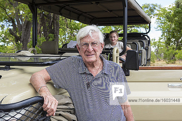 Ein älterer Mann steht lächelnd neben einem Safarijeep.