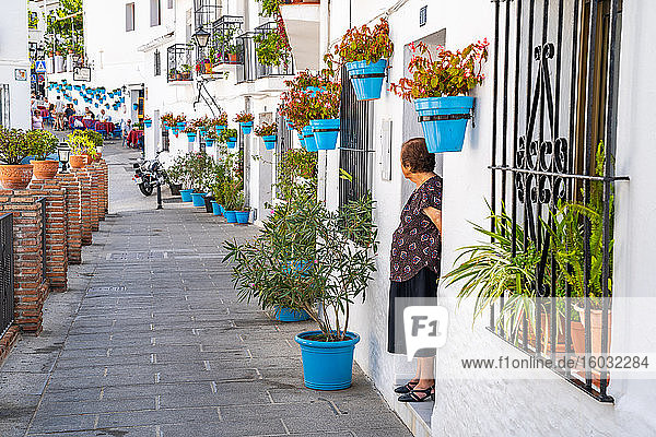 Eine ältere Frau steht vor einem weiss getünchten  mit blauen Pflanzentöpfen bedeckten Haus in Mijas Pueblo  Andalusien  Spanien  Europa