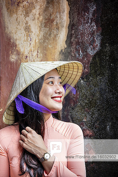 Eine junge Vietnamesin in traditionellem Ao-Dai-Kleid und Kegelhut und lächelnd  Farbton  Vietnam  Indochina  Südostasien  Asien