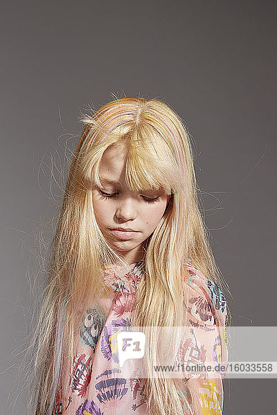 Bildnis eines Mädchens mit langen blonden Haaren  das ein rosafarbenes Rüschen-Pom-Pom-Monsterkleid trägt  auf grauem Hintergrund.