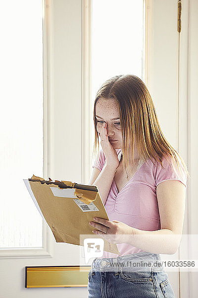 Ein junges Mädchen steht im Flur und hält einen großen Umschlag mit einem Brief in der Hand.