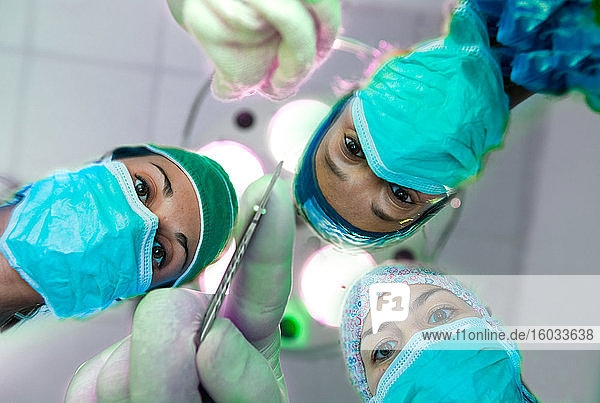 Niedrigwinkelansicht von drei Chirurginnen mit Operationsmasken  die in die Kamera schauen.
