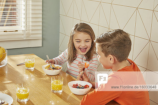 Boy and girl sitting at kitchen table  eating breakfast.