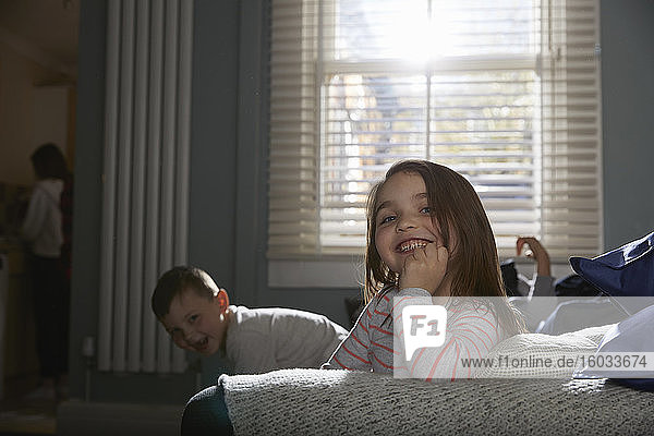 Zwei Kinder sitzen im Schlafanzug auf einem Sofa und lächeln in die Kamera.