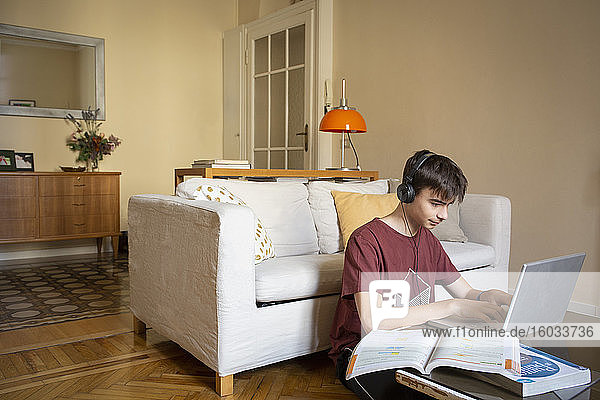 Boy wearing headphones sitting on floor in living room  typing on laptop  studying.