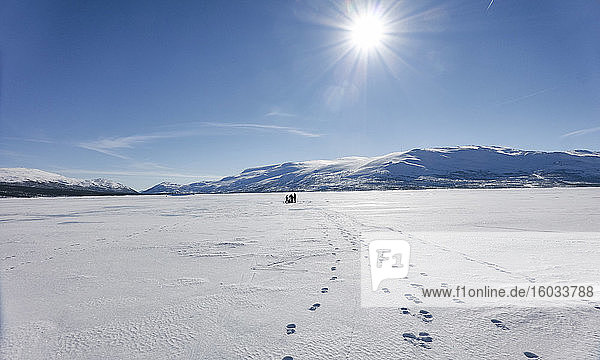 Blick über den gefrorenen See mit Menschen in der Ferne  drei Spuren von Fußabdrücken
