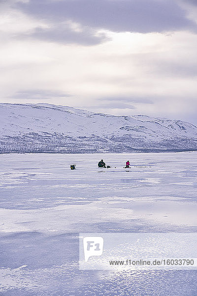 Fernblick von zwei Personen beim Eisfischen auf dem zugefrorenen See in Vasterbottens Lan  Schweden.