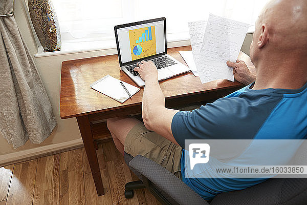 Man sitting using laptop at small desk  working at home during Coronavirus crisis.