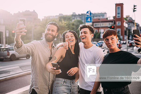 Two young women and men wearing casual clothes standing on a rooftop  taking selfie with mobile phone.