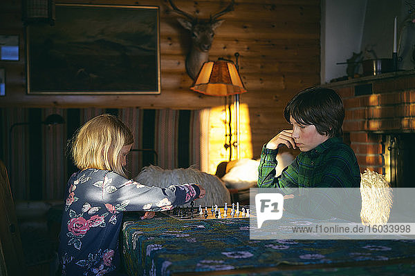 Boy and girl sitting at a table in a log cabin  playing chess  Vasterbottens Lan  Sweden.