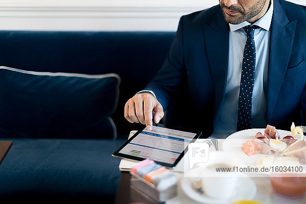 Geschäftsmann schaut während des Arbeitsessens auf sein digitales Tablet.