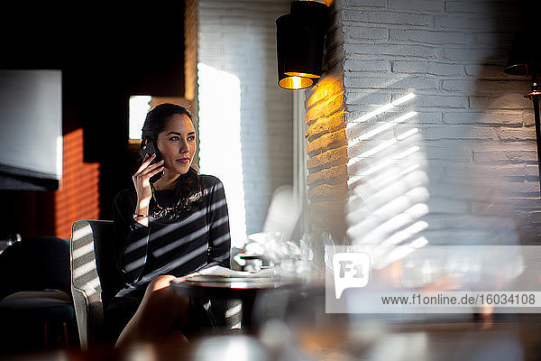 Geschäftsfrau  die an einem Tisch sitzt und ein Mobiltelefon benutzt.