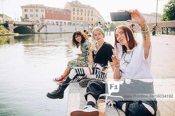 Drei junge Frauen sitzen am Ufer eines Flusses und nehmen Selbsthilfe.