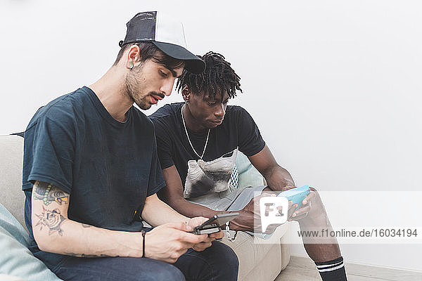 Two young men sitting on a sofa  checking their mobile phones.