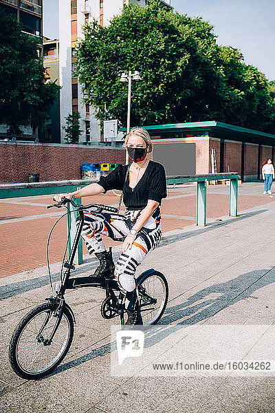 Young woman wearing face mask during Corona virus  cycling on folding bicycle.
