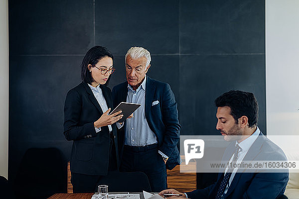 Geschäftsmann und -frau schauen auf digitales Tablet im Sitzungssaal