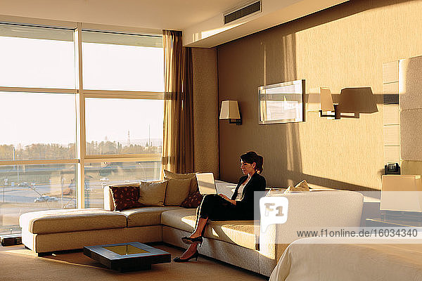 Businesswoman using laptop in lounge area of hotel bedroom