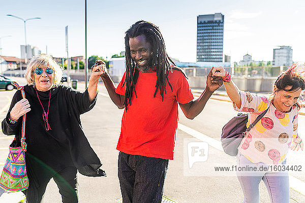 Black man with dreadlocks and two Caucasian women dancing in a street.