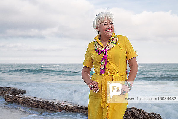 Portrait of smiling woman standing by the ocean  wearing yellow dress.