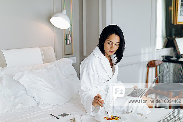 Woman using laptop and having breakfast in suite