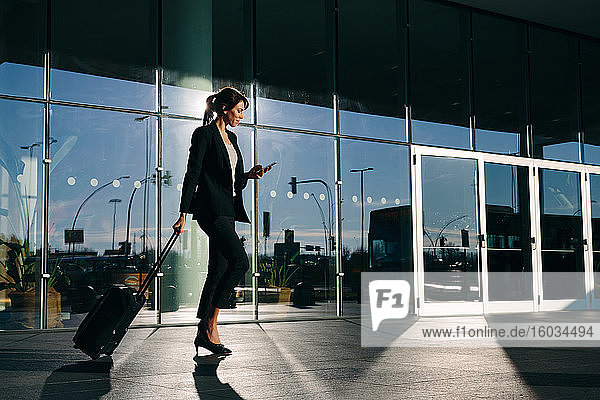 Businesswoman with wheeled luggage passing glass building  Malpensa  Milan