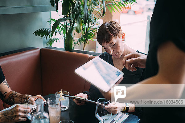 Kellner  der an einem Tisch in einer Bar steht und mit Hilfe eines digitalen Tabletts Bestellungen aufnimmt.