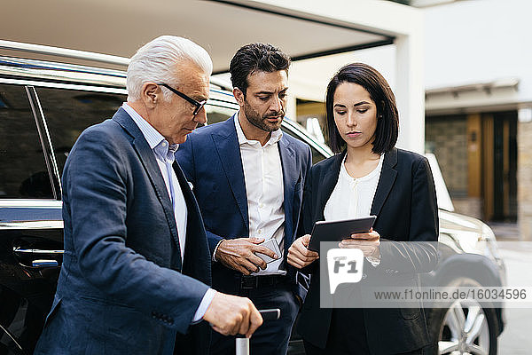 Zwei Geschäftsleute vor einem Hotel mit Blick auf digitales Tablet