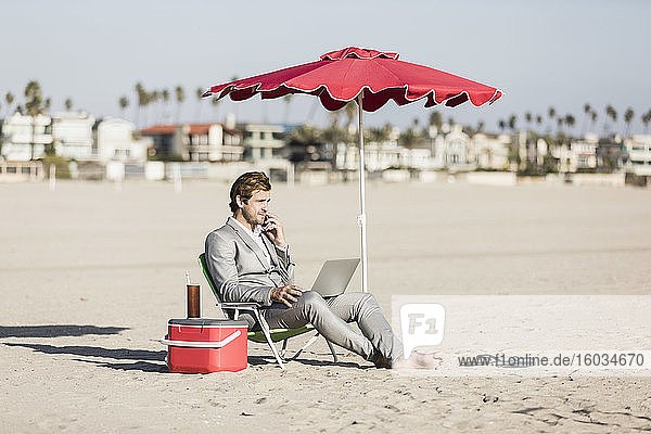 Barfüßiger Geschäftsmann arbeitet am sonnigen Strand  Los Angeles  Kalifornien