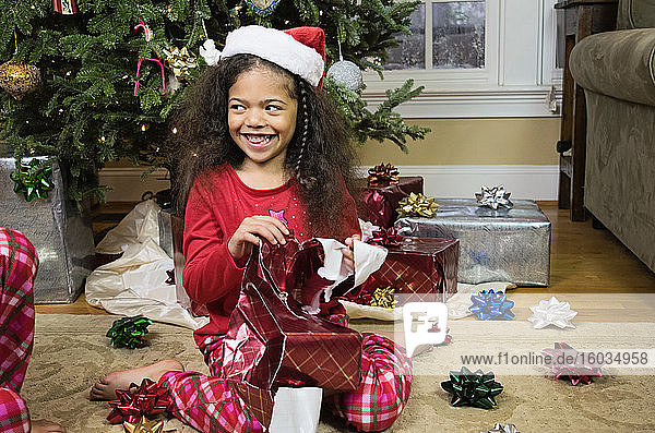 Glückliches Mädchen im Pyjama öffnet Weihnachtsgeschenk am Weihnachtsbaum