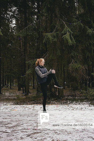 Läuferin beim Beinstrecken in verschneiten Wäldern