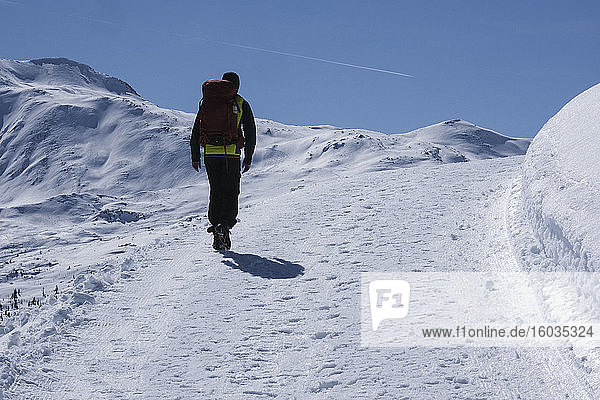 Mann mit Rucksack wandert auf sonnigen  verschneiten Bergweg  Muestair  Schweiz