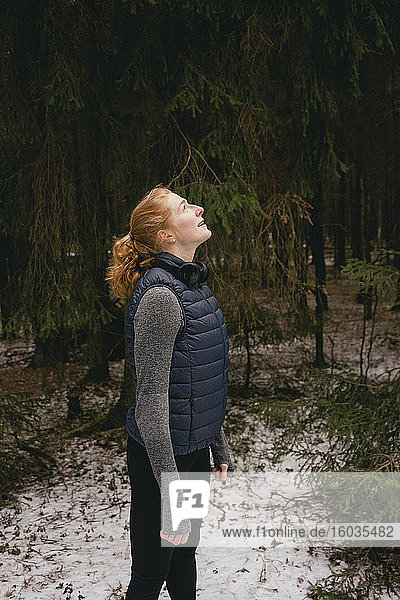 Gelassene rothaarige Frau schaut in verschneiten Wäldern auf