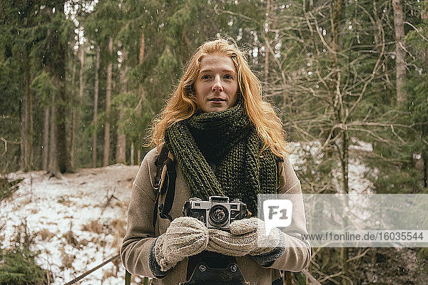 Porträt einer rothaarigen Frau mit Kamera in verschneiten Wäldern