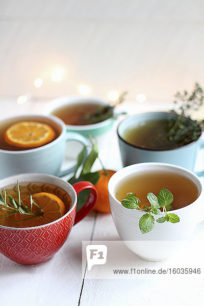 Teetassen mit verschiedenen Kräutern und Orangenscheiben