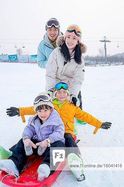 Ski parents pushing children sitting in the snow slide