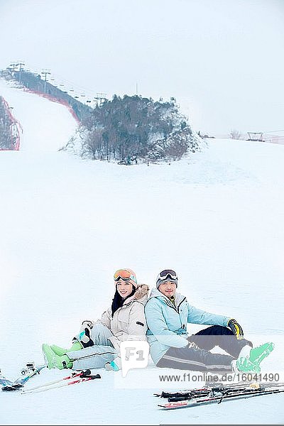 Glückliche junge Paare sitzen Rücken an Rücken im Schnee