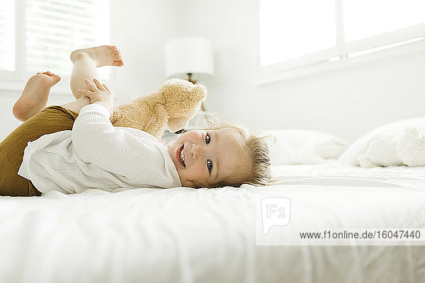 Toddler girl lying on bed with her teddy bear toy