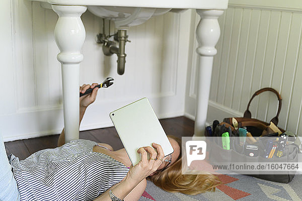 Frau repariert Spülbecken  während sie sich auf dem Laptop ein DIY-Tutorial ansieht