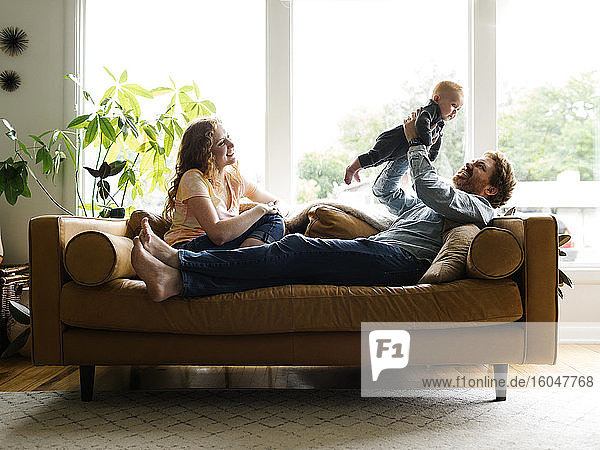 Mutter und Vater spielen mit dem kleinen Sohn (6-11 Monate) auf dem Sofa