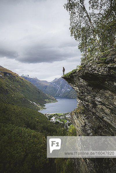 Norwegen  Geiranger  Mann steht am Rand einer Steilklippe über dem Geirangerfjord