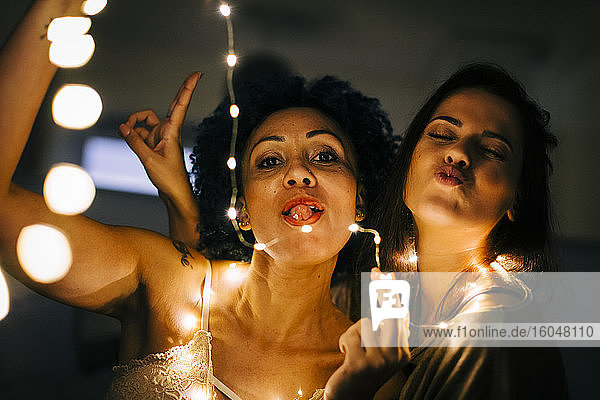 Close-up of female friends with illuminated string lights enjoying at home