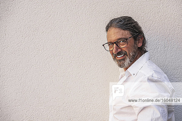 Confident mature man wearing eyeglasses against gray wall