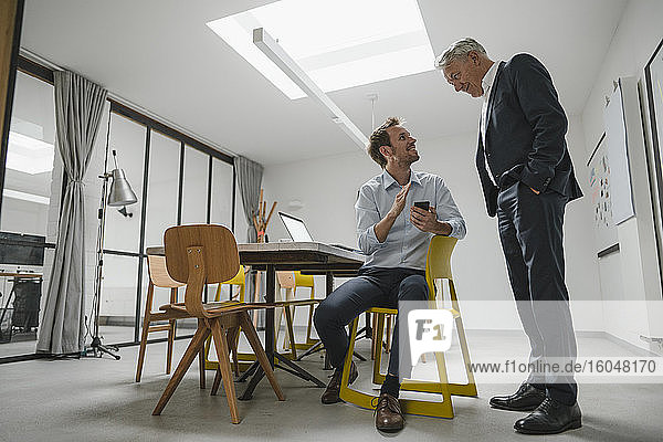 Senior businessman listening to younger business partner  holding smartphone