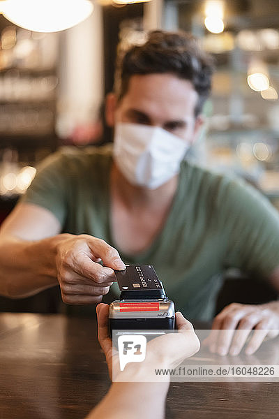 Man with protective mask paying with credit card in restaurant