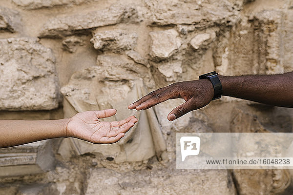 Cropped hands of couple reaching each other against stone wall