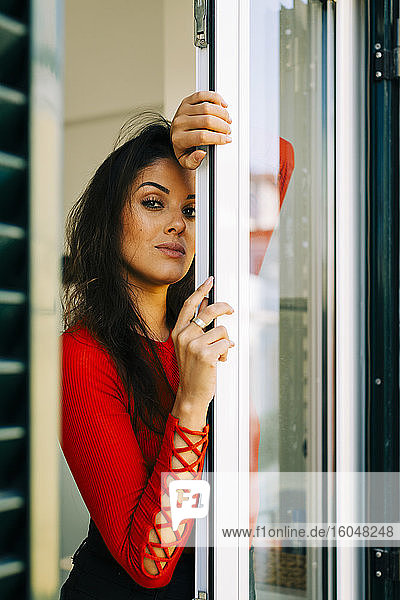 Serious young woman with long hair standing by door at home