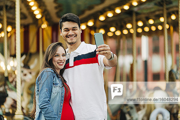 Happy expectant couple taking selfie through smart phone at amusement park  Cascais  Portugal